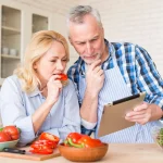 Senior couple checking a meal plan on tablet while cooking.