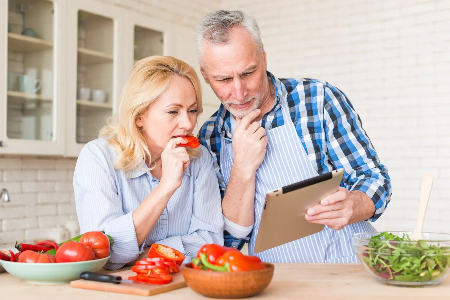 Senior couple checking a meal plan on tablet while cooking.